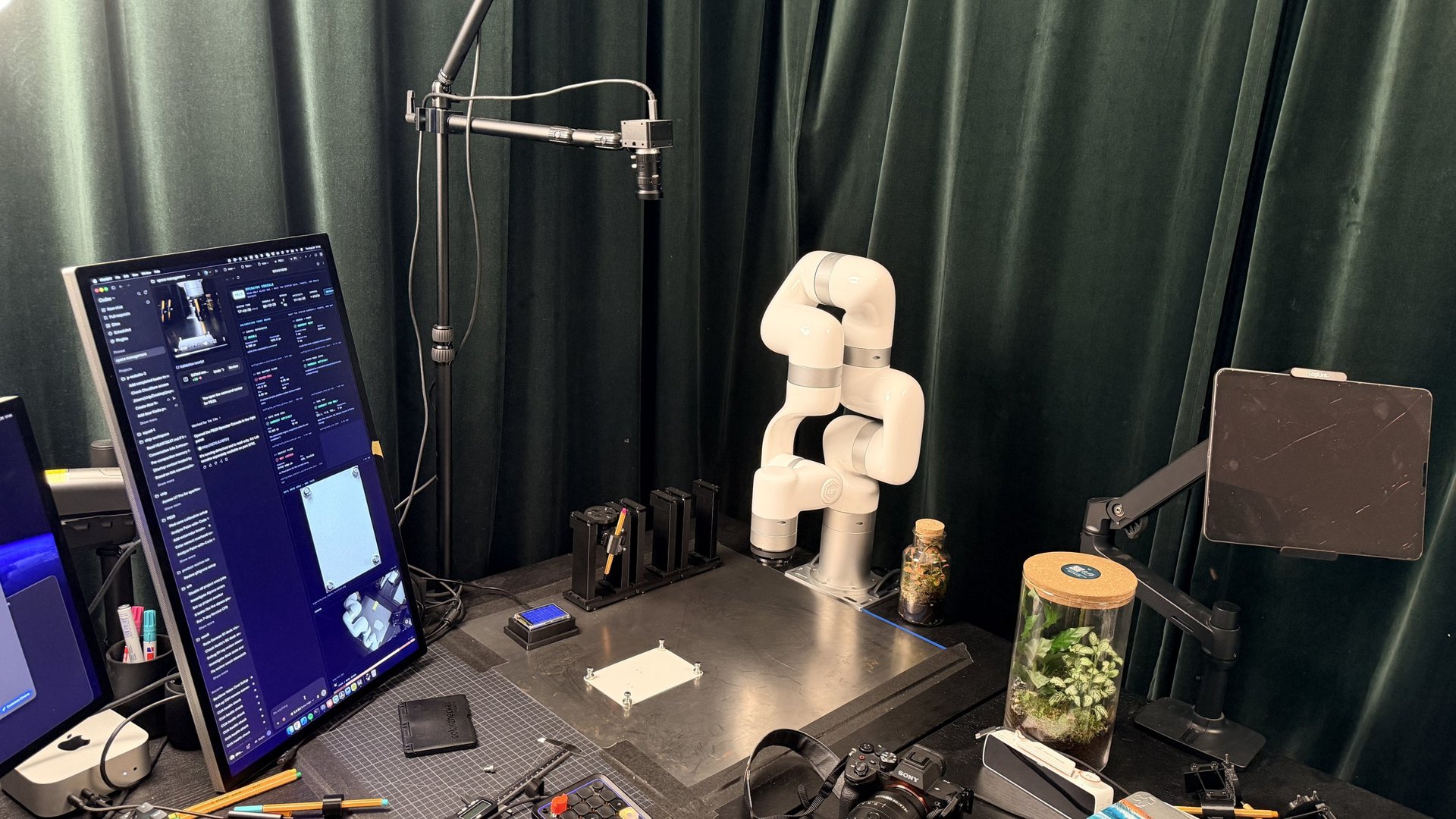 The studio: the white xArm 7 on its table with pen stations, cameras on booms and a monitor running the agent